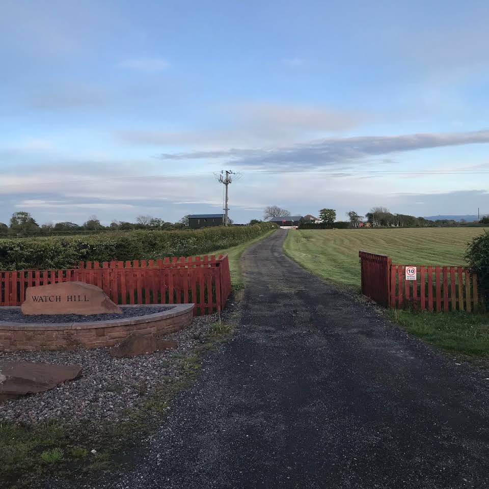 The track into the site between red gates, with fields beyond
