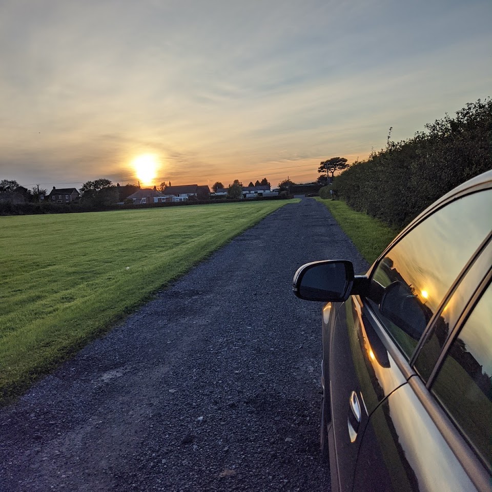 Sunset over the field and the track, with a parked car in the foreground